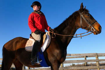 Young female horseback rider in red jacket looking back against a blue sky