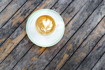 Cup of fresh creamy cappuccino with latte art on foam. Background of wooden table with shabby aged surface. Directly from above.