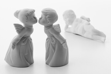 White porcelain boy and girl angels kissing with a third angel lounging in the white background