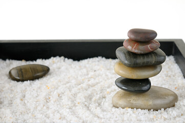Smooth rocks stacked in a miniature raked Zen rock garden sandbox on white background