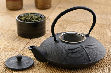 Obraz na płótnie Canvas Japanese cast iron teapot with tea leaves and cups on a handmade maize mat