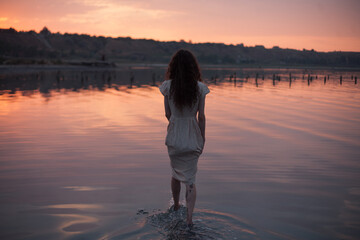 girl in a dress walks in the sunset water