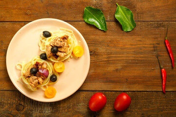 Pink plate with spaghetti nests stuffed with chicken fillet with olives on the table.