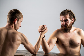 Arm wrestling. Heavily muscled bearded man arm wrestling a puny weak man. Arms wrestling thin hand,...