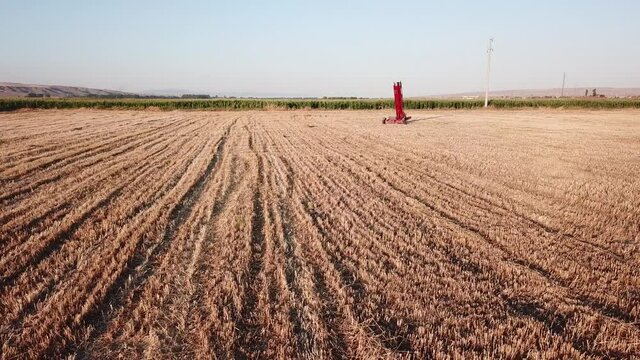 Aerial view of the gold color hay field. Hay baler machine can be seen in the middle of field.  