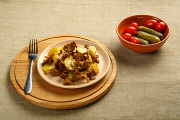 potatoes with mushrooms larvae on a round delivery and a fork next to pickled cucumbers and tomatoes.