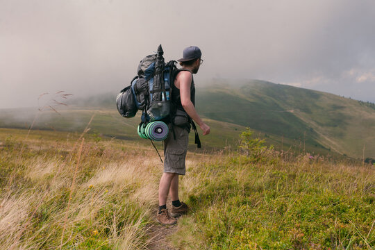 photo of a guy in camping equipment on a background of clouds and mountain peaks