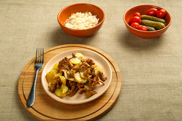 potatoes with mushrooms larvae on a round delivery and a fork next to pickled cucumbers and tomatoes and cabbage.