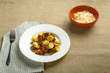 a plate of potatoes with mushrooms larvae on a napkin and a fork next to pickled cabbage.