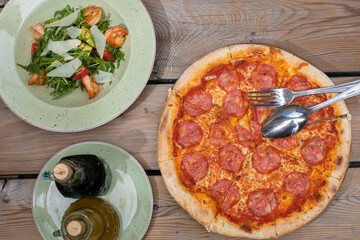 Italian food. Peperoni pizza and shrimp caesar salad. There is oil and balsamic vinegar nearby. Wooden table. Lunch on the summer terrace in the cafe. Italian pizza.