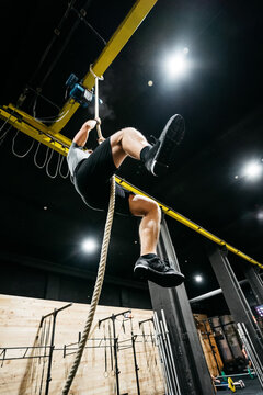 Athletic man climbing a rope in a crossfit box