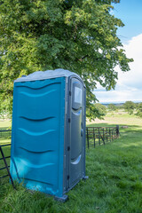 A single plastic blue portable toilet in a field at an outdoor event in England