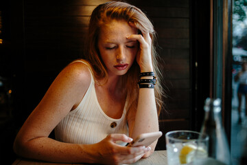 Red-hair young woman looking at her phone in a bar.