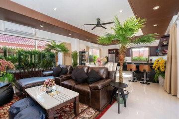 Interior design of house, home, villa feature leather couch, black sofa cushion, artificial flower on the table, cabinet and a view of garden from living room