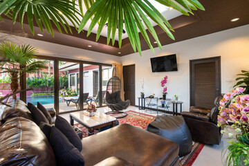 Interior design of house, home, villa feature leather couch, black sofa cushion, artificial flower on the table, television, egg shape chair swing and a view of swimming pool from living room
