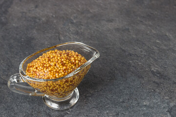 French mustard in a glass sauceboat on a black background. Dijon mustard