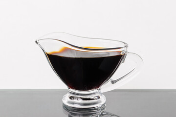 soy sauce in a glass gravy boat on a black table on white background. dish of soy sauce on glass black table