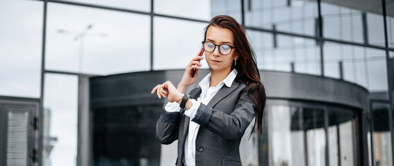 A business woman checks the time and talking on the phone in the city during a working day waiting for a meeting. Discipline and timing. An employee goes towards a corporate meeting.