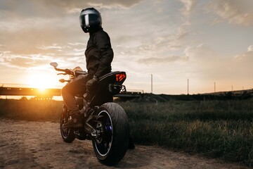 Back view of biker sitting on motorcycle in sunset on the country road.