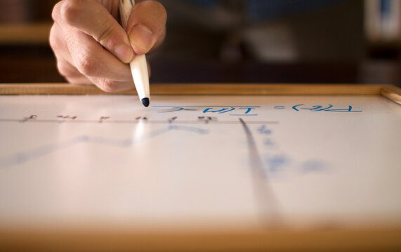 man's hand writing formulas on the blackboard