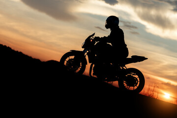 Silhouette photo of biker driving motorcycle in sunset on the on mountainous road. Success and victory concept.