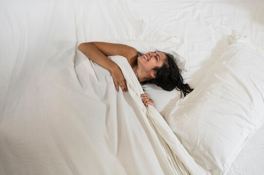 Happy young woman wrapped in white sheets in the bed