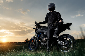 Photo of biker sitting on motorcycle in sunset on the country road. © Screaghin