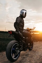 Dramatic image of biker sitting on motorcycle in sunset on the country road.