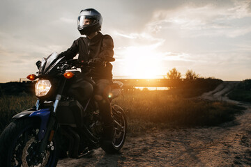 Close-up photo of biker sitting on motorcycle in sunset on the country road. Copy space.