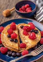 Sliced sweet homemade pancakes with raspberries and blueberries on blue plate.