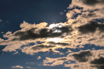 Dark blue sky with fantastic clouds. Sun is shining from behind the clouds.