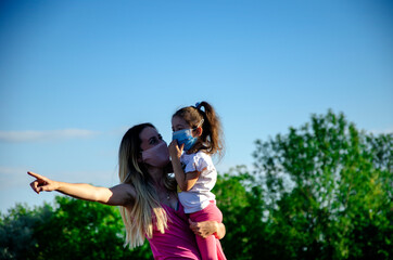 Fototapeta premium Little child with mom wearing medical masks. Mom and daughter are having fun in the summer. Kid with mom on self-isolation have a happy time