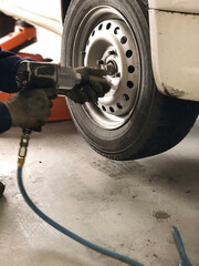 Auto mechanic man with electric screwdriver changing tire outside. Car service.  Tire installation concept. Replacement of winter and summer tires. Hands replace tires on wheels.