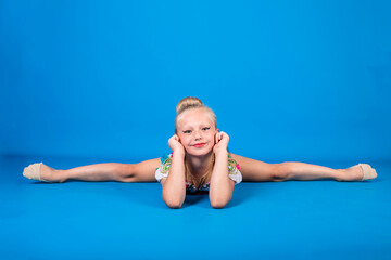 A beautiful gymnast sits in a cross split and looks at the camera on a blue isolated background with space for text