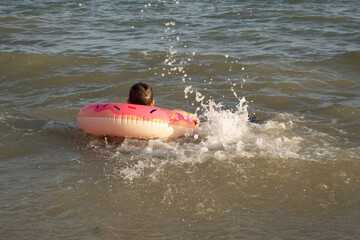 Naklejka premium A cheerful boy 5 years old swims in the sea on an inflatable ring in the form of a donut on a sunny day.