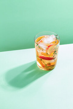 Sparkling cold brew peach tea with thyme in glass on green paper background. Refreshing summer non-alcoholic drink concept
