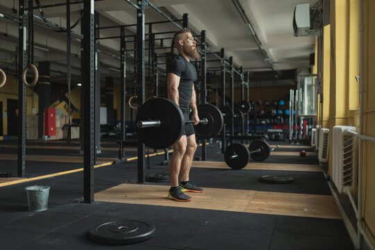 Strong and healthy man workin out with bar and weights inside a crossfit gym.