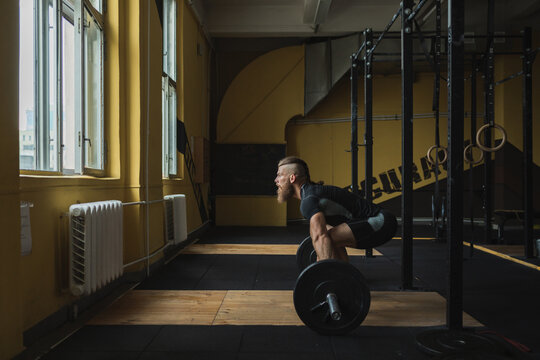 Strong and healthy man workin out with bar and weights inside a crossfit gym.