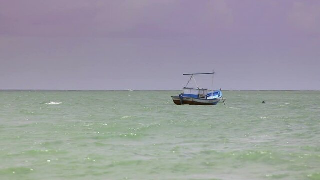 Artisanal fishing boat anchored on Coroa Vermelha beach, sea with maoras, cloudy sky