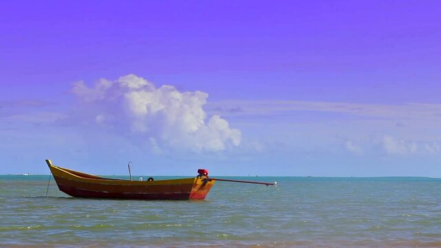 Bucolica image of handmade fishing boat, painted in red and yellow tones, anchored on Coroa Vermelha beach, sea with ripples, cloudy sky