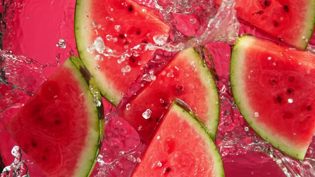 Super Slow Motion Shot of Falling Fresh Watermelon Slices into Water on Red Background at 1000fps.