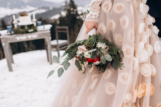 Beautiful winter bouquet in the hands of the bride. Bride holding her bouquet. dridal bouquet of roses with pine, branches of eucalyptus, succulents and pine cone in women's hands