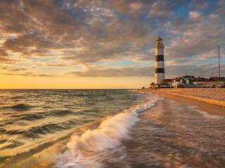 view to sea and waves on the beach in front of old lighthouse at sunset time with copy
