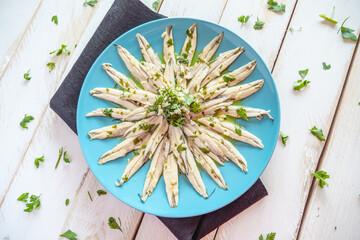  Pickled anchovies with garlic and parsley marinated in vinegar in a round wooden plate on a white wooden table. Typical Spanish snack. 
