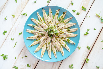  Pickled anchovies with garlic and parsley marinated in vinegar in a round wooden plate on a white wooden table. Typical Spanish snack. 