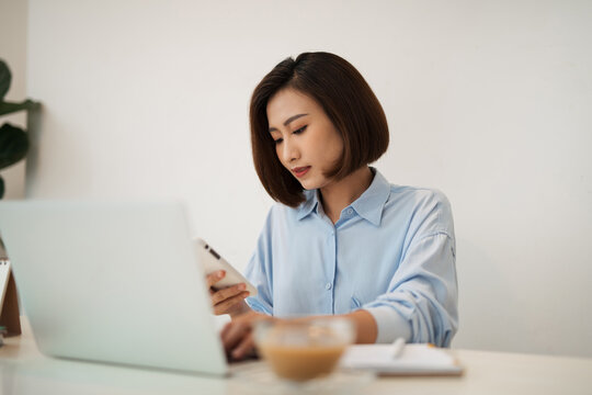 Shot of an thinking asian woman using a mobile phone and laptop
