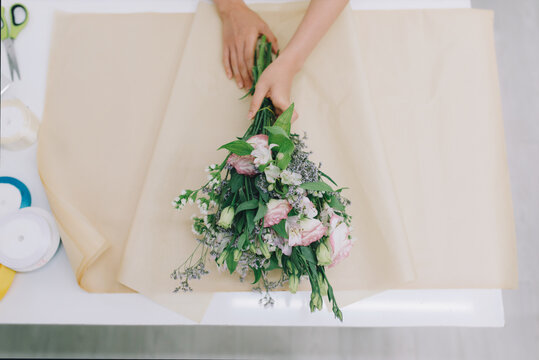 cropped image of florist wrapping bouquet in pack paper in shop