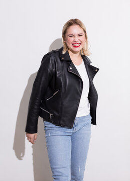 Beautiful blonde plus size woman in jeans and a leather jacket laughs on a white background