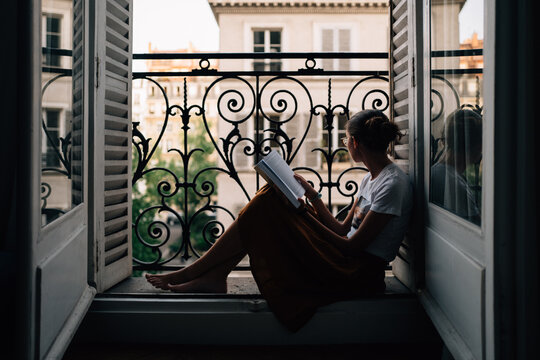Girl looking out of apartment in Paris, while reading book.