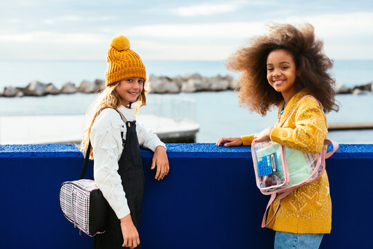 Cheerful diverse girls resting on embankment after school